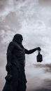 From below of aged stone statue of male with lantern under cloudy sky in night city