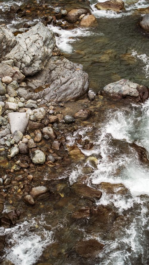 Free From above of wavy sea water flows with foam against coast with rough stones in daytime Stock Photo
