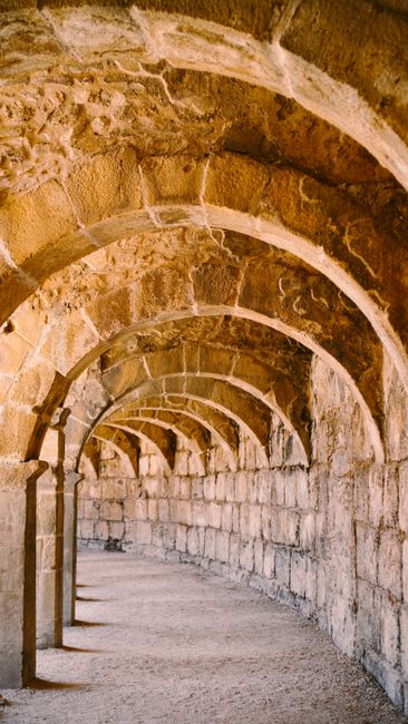 Empty wavy walkway with arches and rough stone wall against columns of old construction in daylight