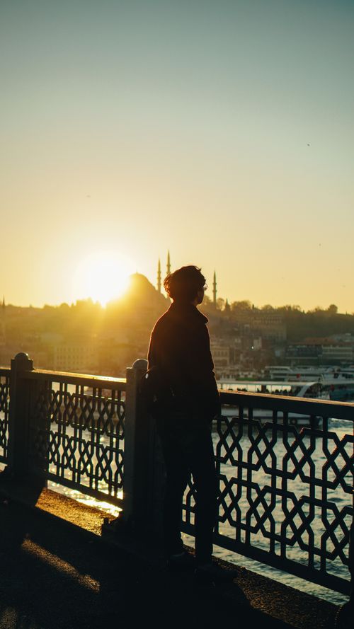 Free Back view of anonymous male admiring shiny sun in night sky while standing on fenced embankment against city harbor Stock Photo