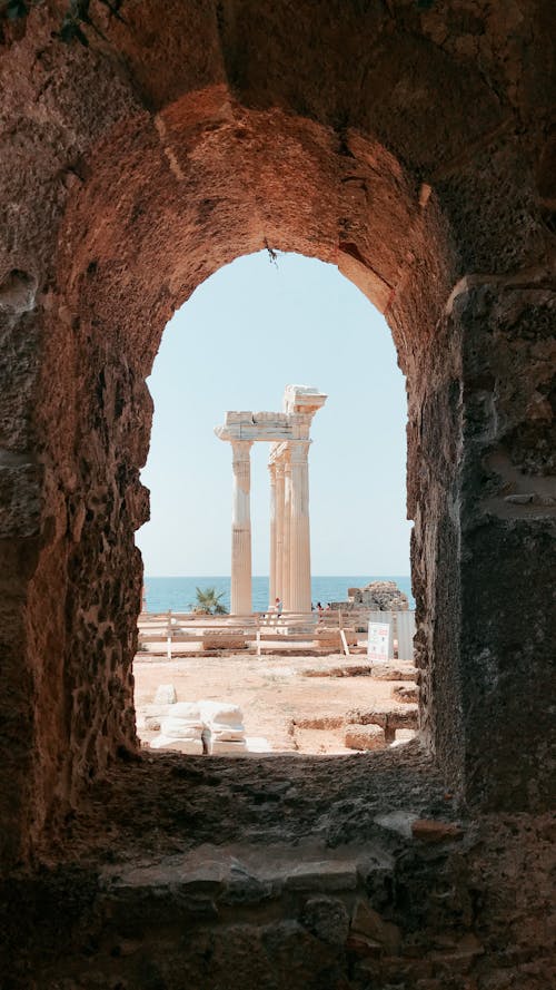 Free View through arched stone passage leading to ruined columns of ancient stone building located on coast of sea Stock Photo