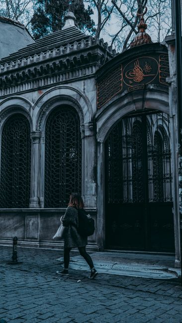 Full body side view of female pedestrian walking on paved walkway near aged arched gates