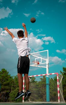 Teen boy shoots basketball on an outdoor court against a clear blue sky in Segovia, Spain.