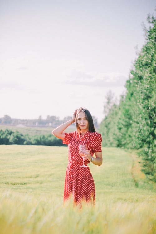 A Woman with Red Dress Holding a Wine Glass in the Countryside Farm