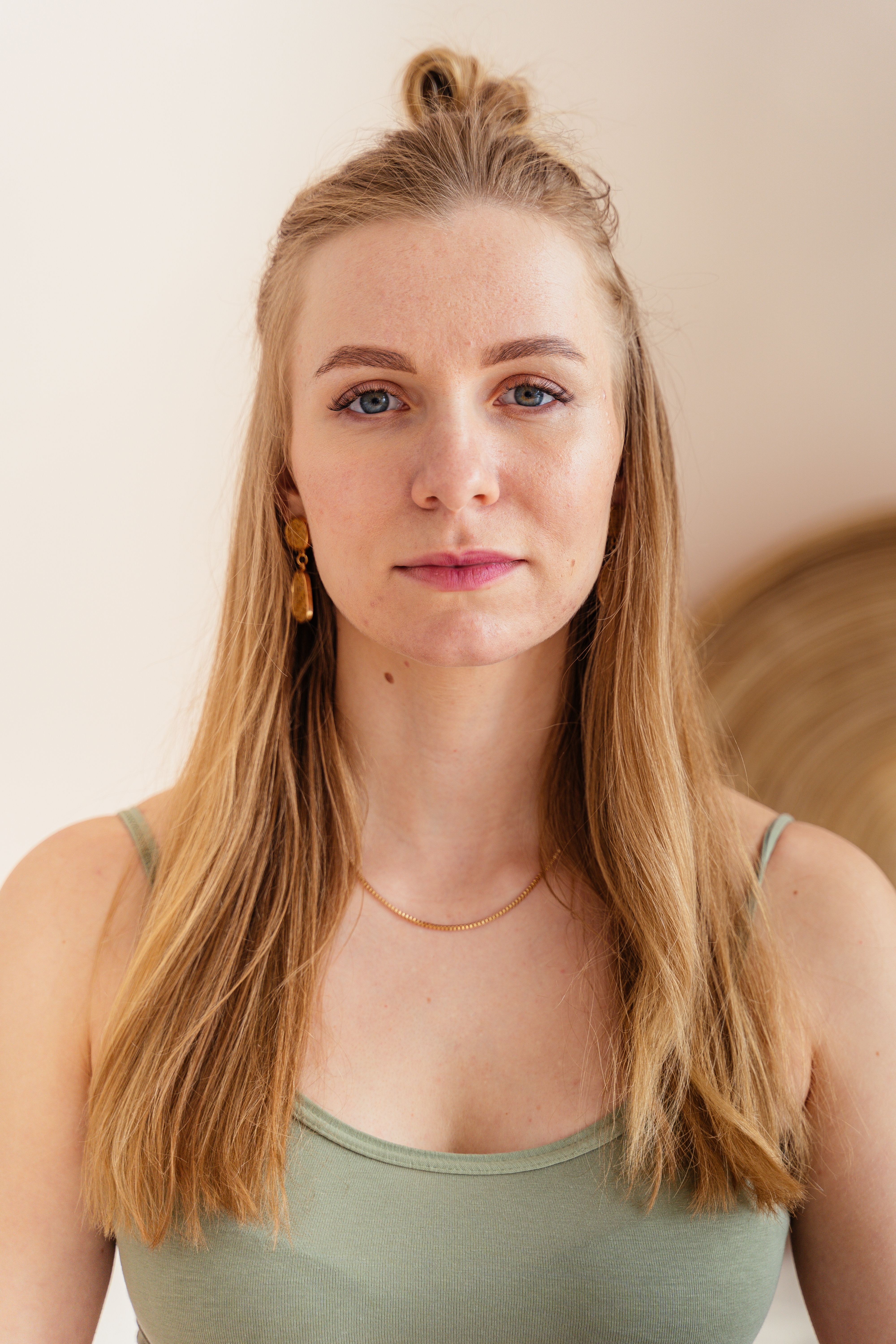 Close-up portrait of a blonde woman wearing a tank top in a warm, neutral setting.