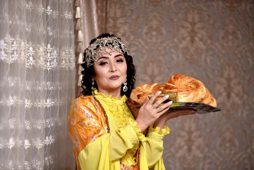 Free Woman in traditional attire holding bread on a tray indoors, showcasing cultural elegance. Stock Photo