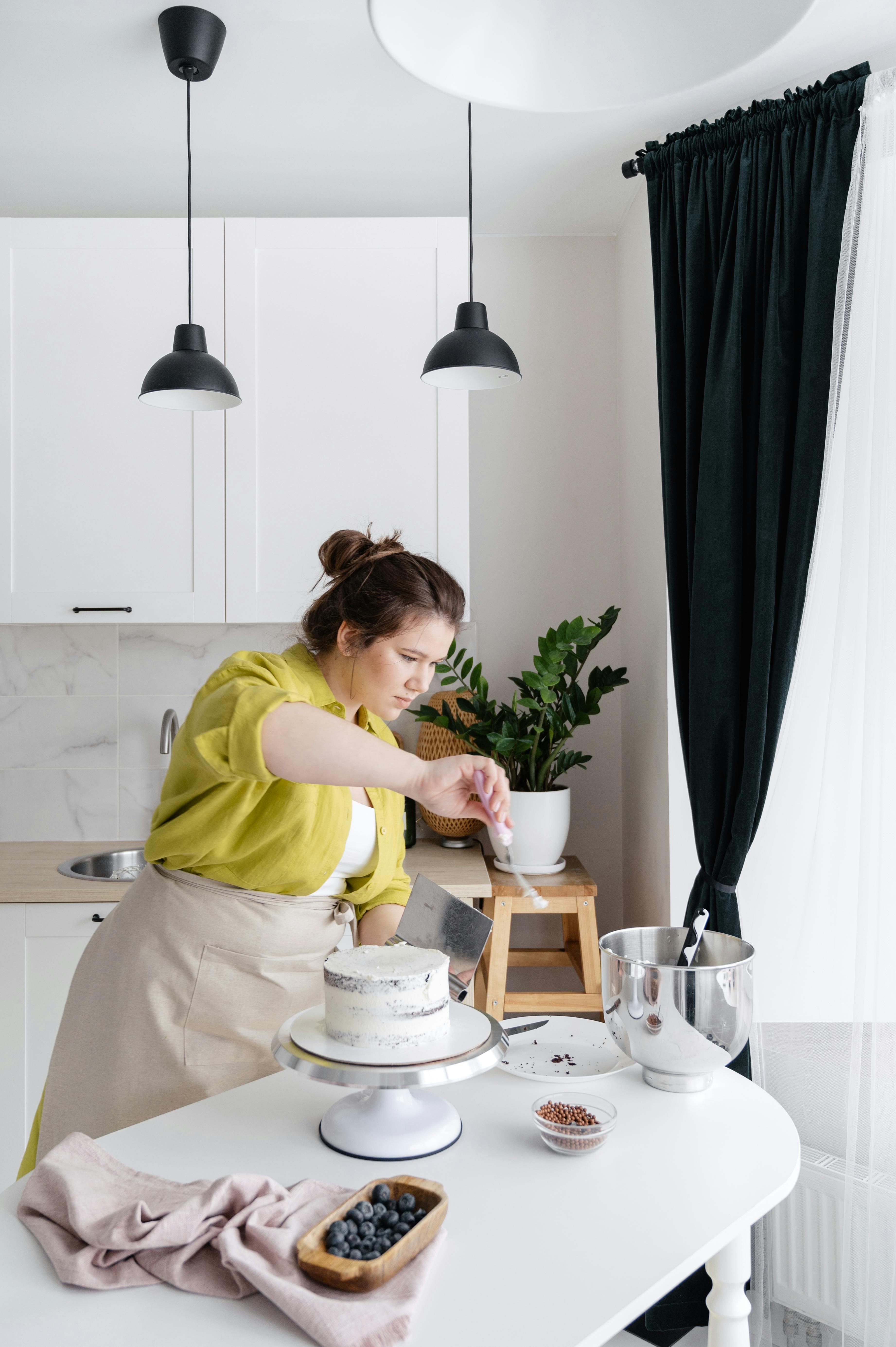 High angle of concentrated female chef preparing tasty cake on table in modern kitchen of white and black color