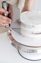 Crop unrecognizable confectioner standing at table while making delicious cake placed on white table in light kitchen