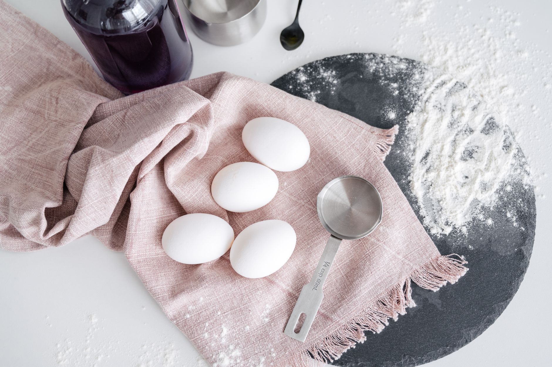 Top view of eggs placed on pink cloth on white table with flour and ladle in kitchen