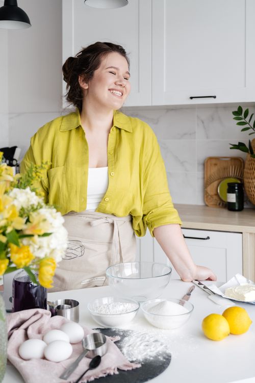 Free Happy young female in apron standing against table with flour in bowl and fresh lemons at home Stock Photo