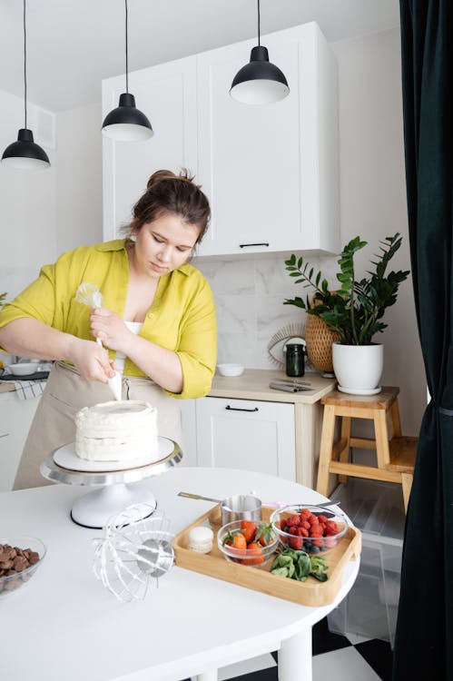 Woman in Yellow Long Sleeve Shirt Decorating a Cake