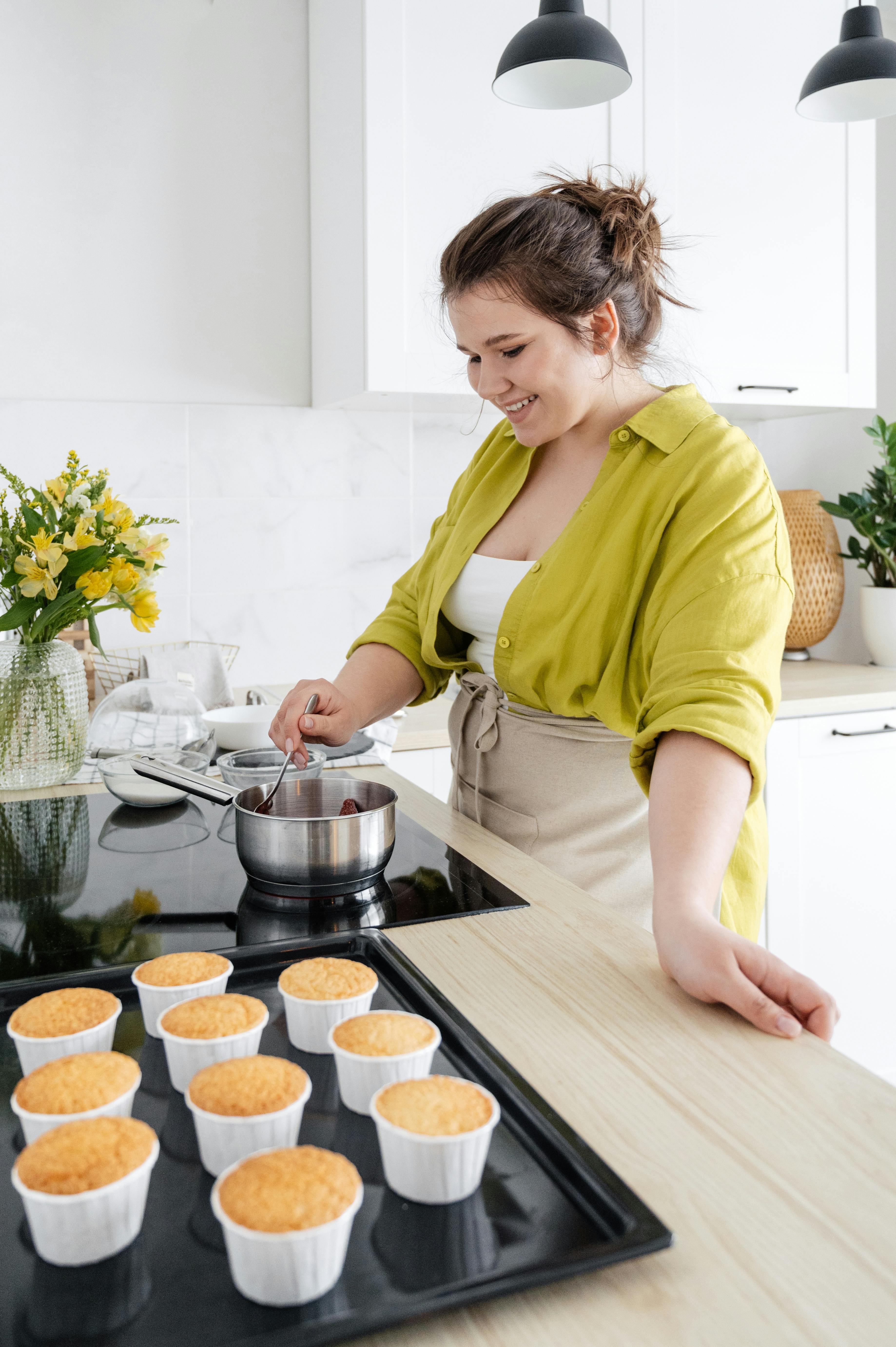 smiling woman preparing delicious jam on stove for baked cupcakes