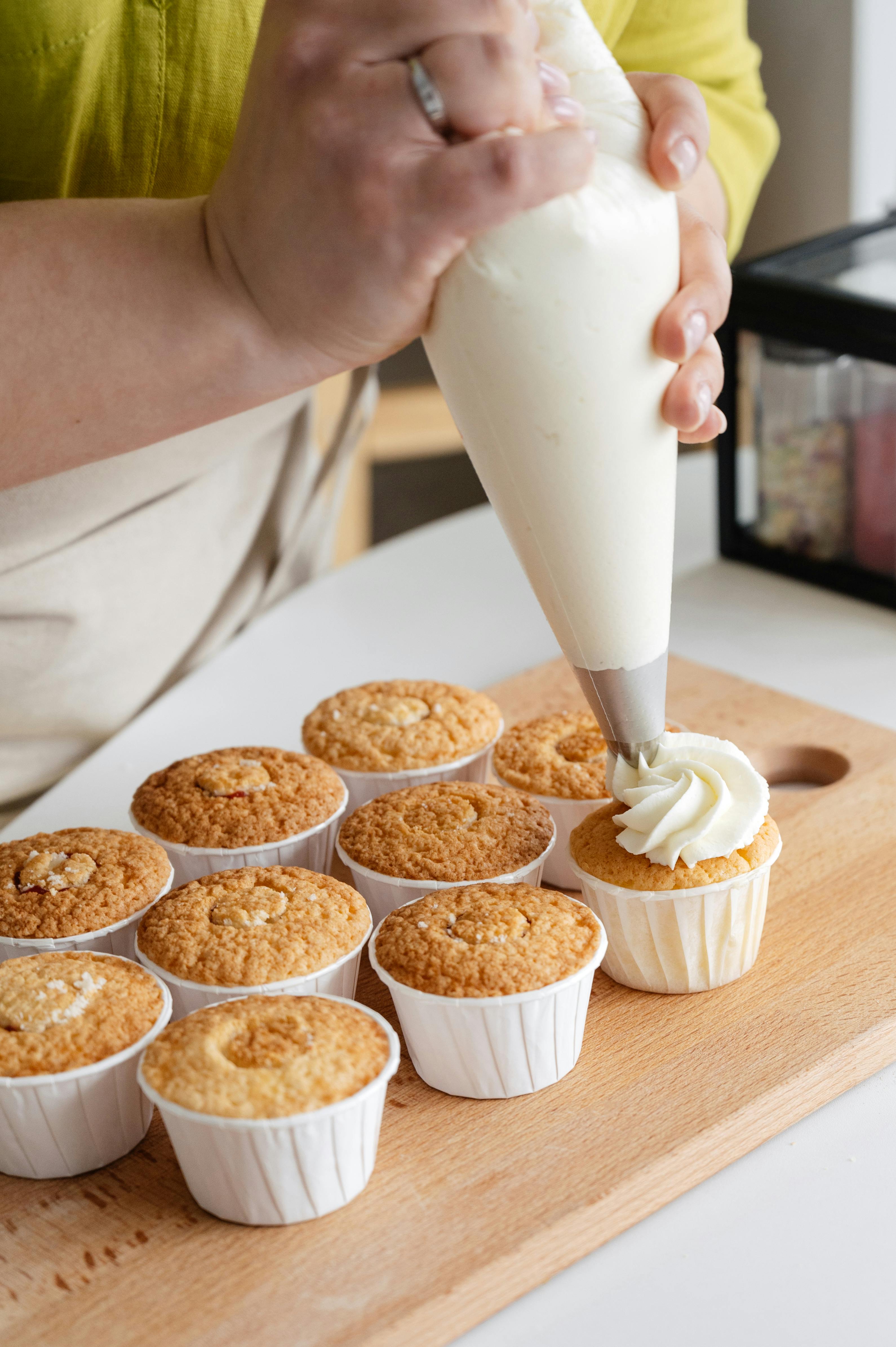 crop cook squeezing cream on cupcakes