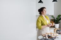 Female cook standing near table and looking away while preparing tasty cupcakes in light kitchen