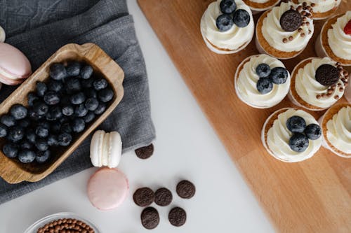 Free Top view of homemade cupcakes served on wooden tray near chocolate sweets and macaroons with blueberries in wooden container Stock Photo
