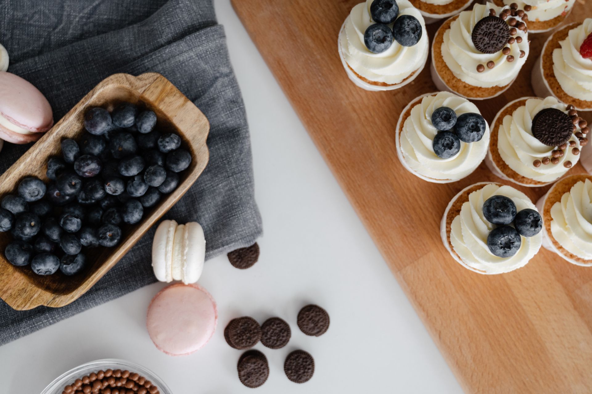 Top view of homemade cupcakes served on wooden tray near chocolate sweets and macaroons with blueberries in wooden container