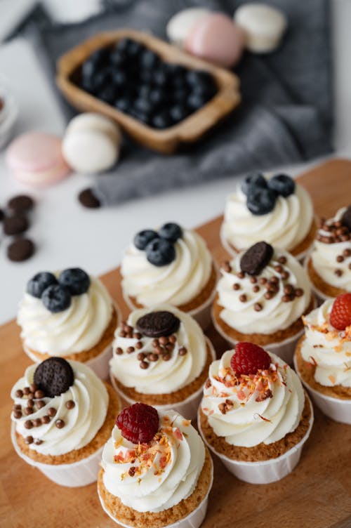 From above of delicious sweet cupcakes with cream and berries on top placed on table against blurred background