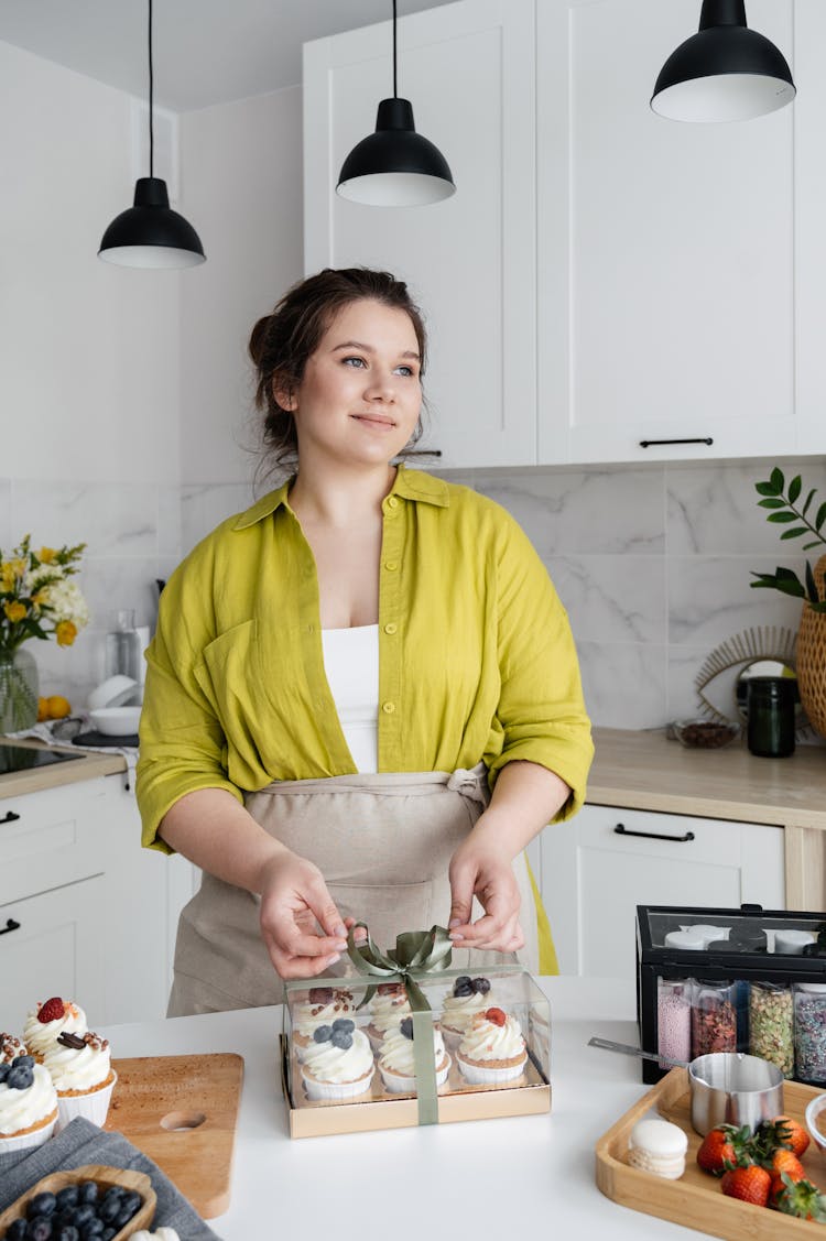 Woman Tying Bow On Transparent Box With Cupcakes