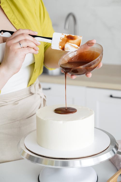 Crop woman decorating cake with chocolate