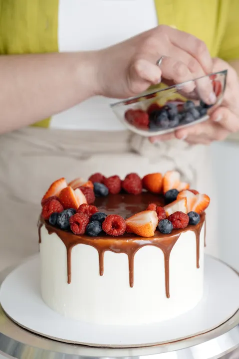 How to Bake Without Eggs: 8 Substitutes That Work for Indian Bakers (2026) 3 A professional baker decorating a finished eggless cake with fresh berries on a revolving stand, showing the quality achievable with egg substitutes.