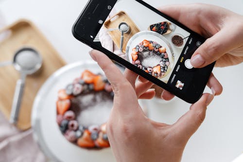 Woman hand taking photo on smartphone of delicious decorated cake