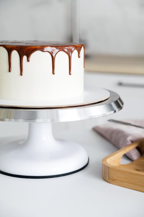 Appetizing tasty biscuit cake decorated with chocolate frosting placed on round stand on kitchen table