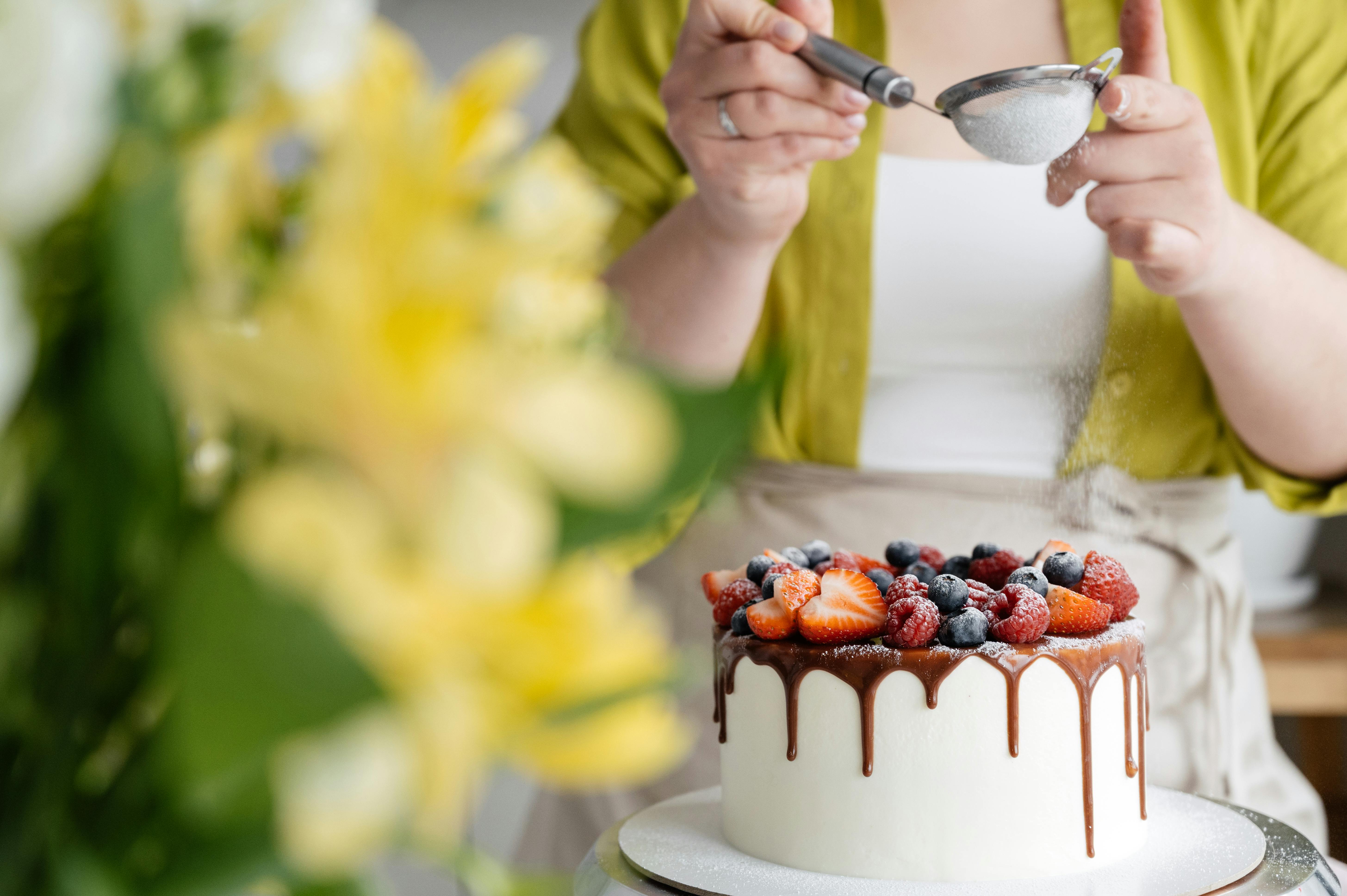 crop female baker strewing powdered sugar to decorated cake