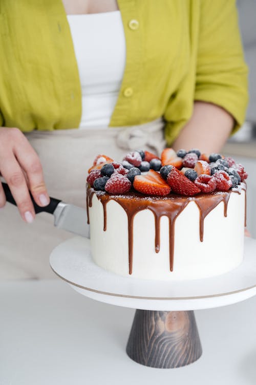 Anonymous lady cutting yummy berry cake in kitchen