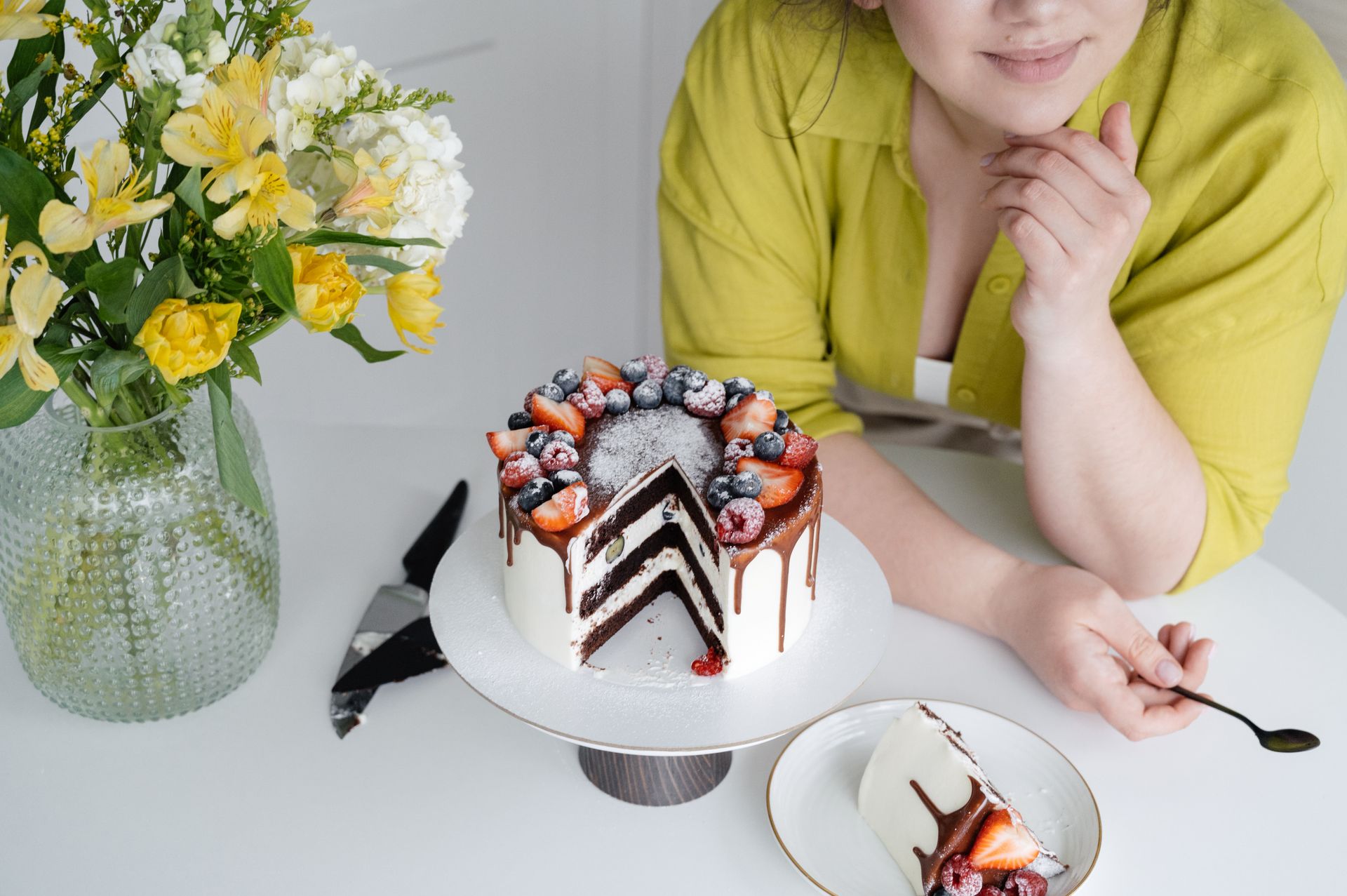 Crop unrecognizable woman smiling and eating berry cake in light kitchen