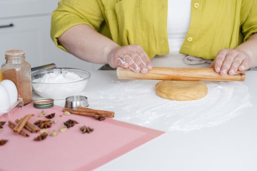 Crop anonymous female sitting at white table and preparing dough for cookies near fresh ingredients in kitchen
