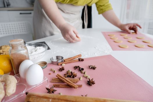 Crop unrecognizable female cook putting unbaked cookies into baking paper placed on white table near bowl with flour and spices and eggs