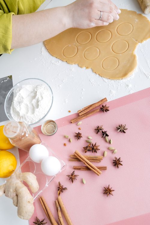 Free From above of crop anonymous female cutting dough for cooking on table near flour and eggs and cinnamon sticks Stock Photo