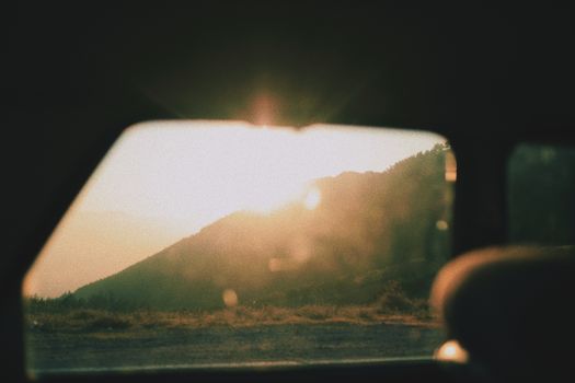 Golden sunset seen through a car window, capturing the serene landscape and warm glow.