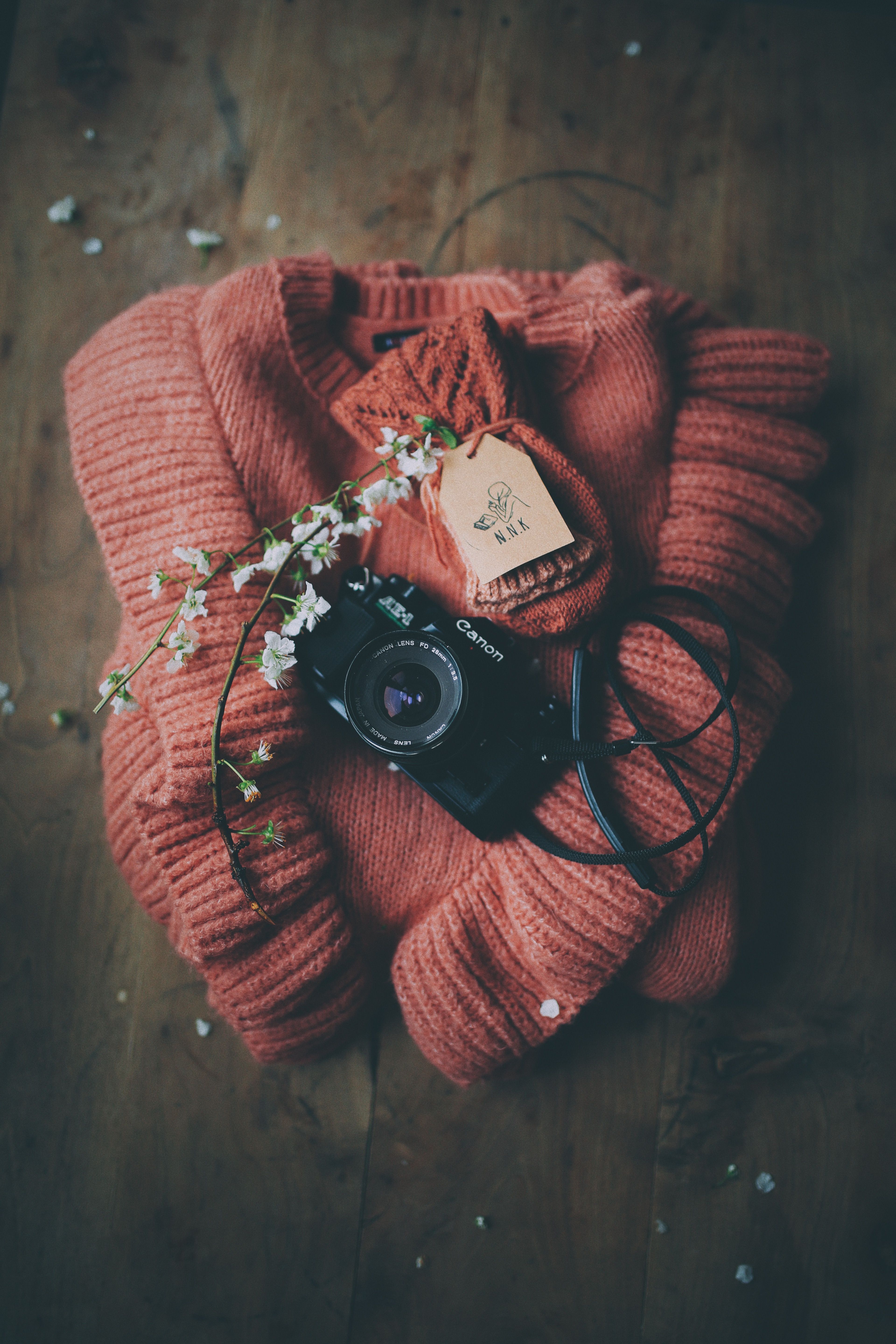 A Canon camera lies on a warm, folded sweater with floral accents, creating a cozy vibe.