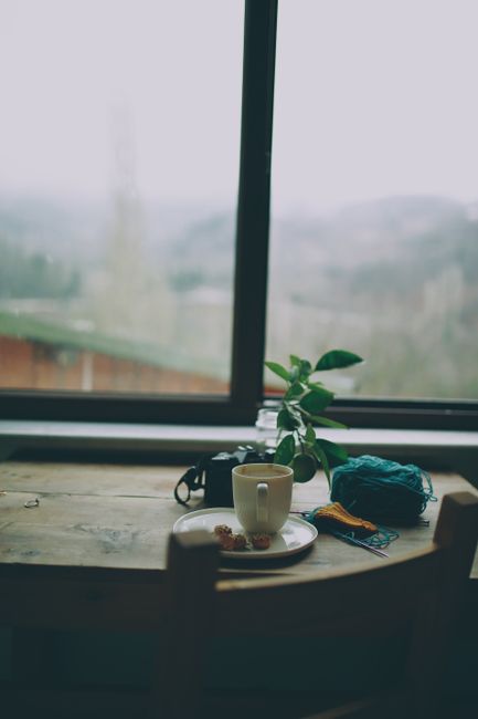 Ceramic cup of coffee placed near ball of yarn on wooden table against window in daytime