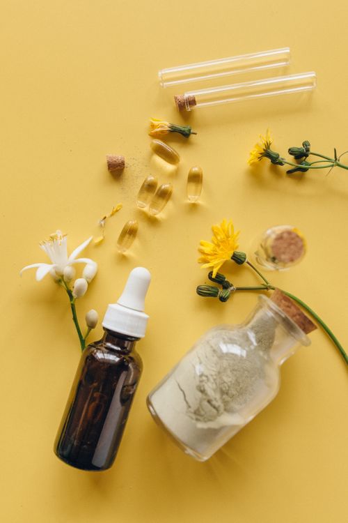 Free Glass bottles with herbs and capsules on a bright yellow surface for wellness concept. Stock Photo