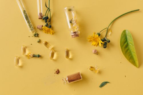 Free A flat lay of glass bottles, capsules, and flowers on a vibrant yellow surface, representing natural remedies. Stock Photo