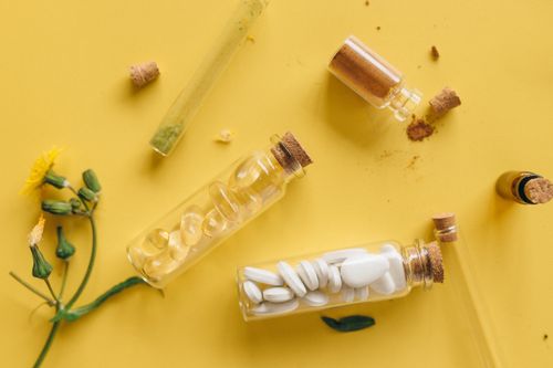 Free Top view of medicinal herbs, pills, and powders in bottles against a vibrant yellow backdrop. Stock Photo