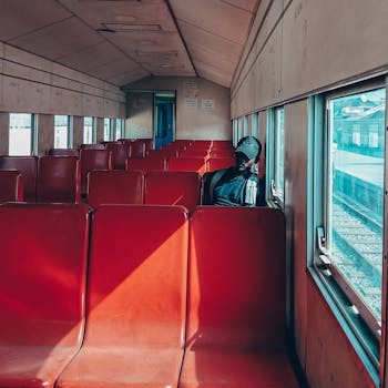African American man sitting alone in an empty train car with red seats, looking out the window.