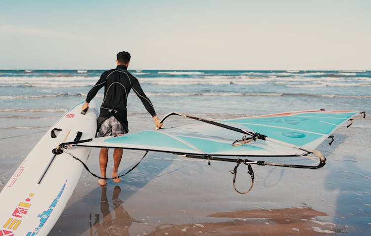 Man Carrying A Surfing Board On The Beach