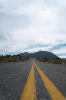 Empty road with yellow lines stretching to distant mountains under a cloudy sky, perfect for travel or adventure themes.