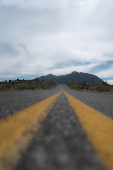 A quiet road with yellow lines leading towards distant mountains under a cloudy sky.