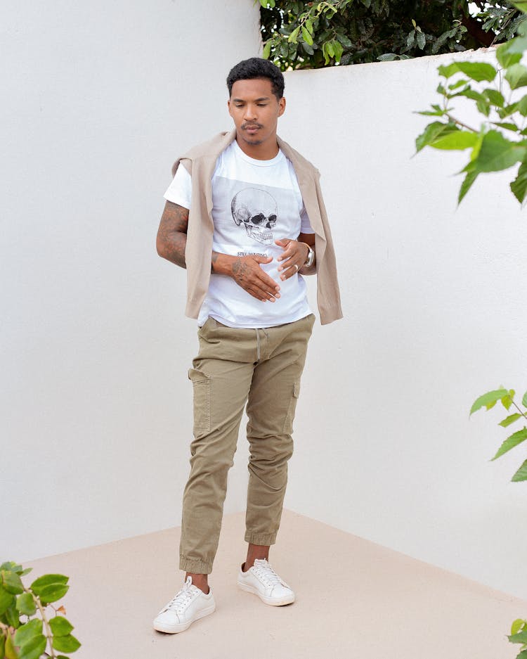 Trendy Young Ethnic Man Standing Near White Wall Near Green Plants