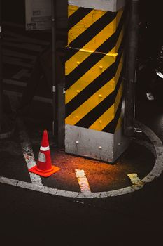 Traffic cone and yellow hazard stripes on a city street corner at night.