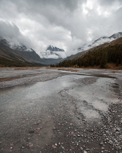 Shallow river against high ridges under cloudy sky