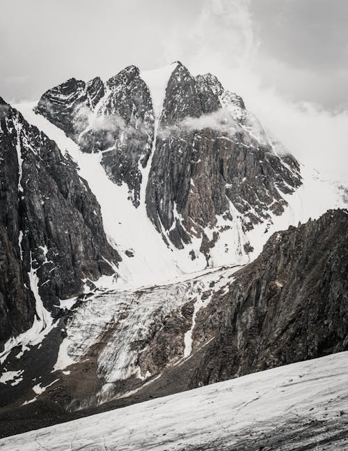 Scenic view of rugged mount with snow and icy waterfall under cloudy sky in misty weather
