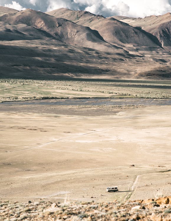 Scenic view of transport driving on dry land against majestic mounts and shallow river on sunny day