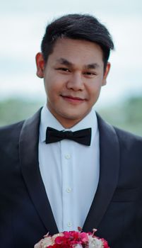 一个穿着燕尾服、面带微笑的男人在户外手持花束的时尚肖像