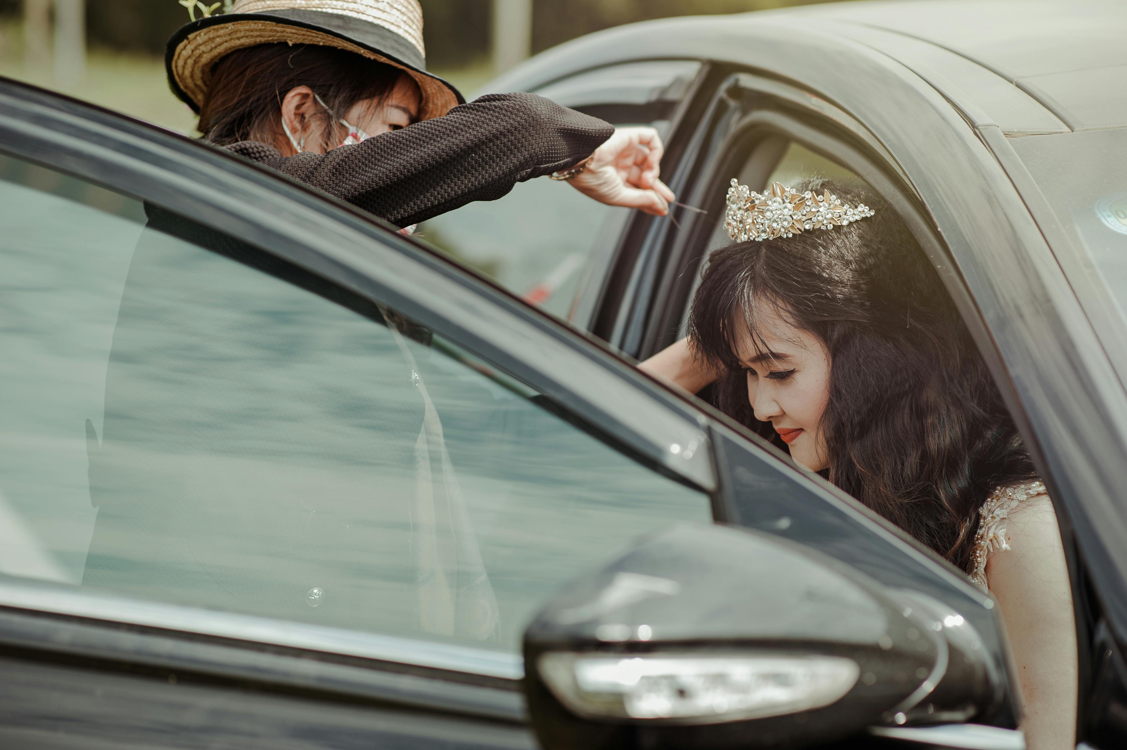Close-up of a woman in a crown and dress getting into a car with assistance outdoors.