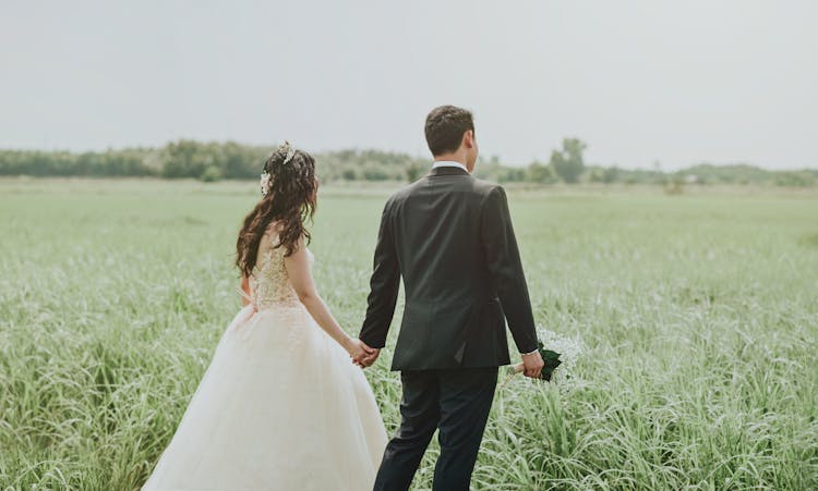 Woman In White Wedding Dress Holding Hand To Man In Black Suit